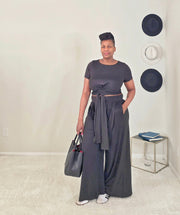 Woman in a black 2 piece outfit standing in a room with a white wall and decorative plates.