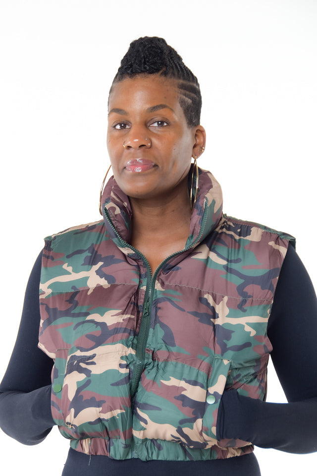 Camo Print Puffer Jacket  Stay stylish and warm with our trendy camo print puffer jacket. This crop jacket combines fashion and function, making it a must-have for any wardrobe.  Key Features:  Crop Design: The cropped length adds a modern and edgy touch to your outfit. Cinched Waist: A cinched waist enhances your silhouette, providing a flattering fit. Side Pockets: Convenient side pockets offer practicality and style. Zip Up: The zip-up front ensures easy wear and a snug fit. Sleeveless: 